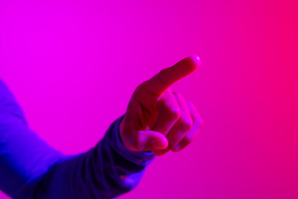 hand of biracial businessman pointing with copy space on neon pink to purple background. technology, digital networks, global connections and communication metaverse.